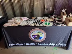 Handcrafted jewelry and baskets displayed on a table with an educational organization's logo and slogan.