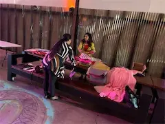 Two women setting up a colorful display table indoors, with pink fabric and clothes.