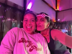 Two people smiling at a lively event with colorful lighting and decorations.