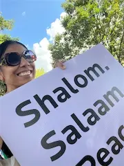 Person holding sign with Shalom, Salaam, Peace promoting unity and peace outdoors under a clear sky.