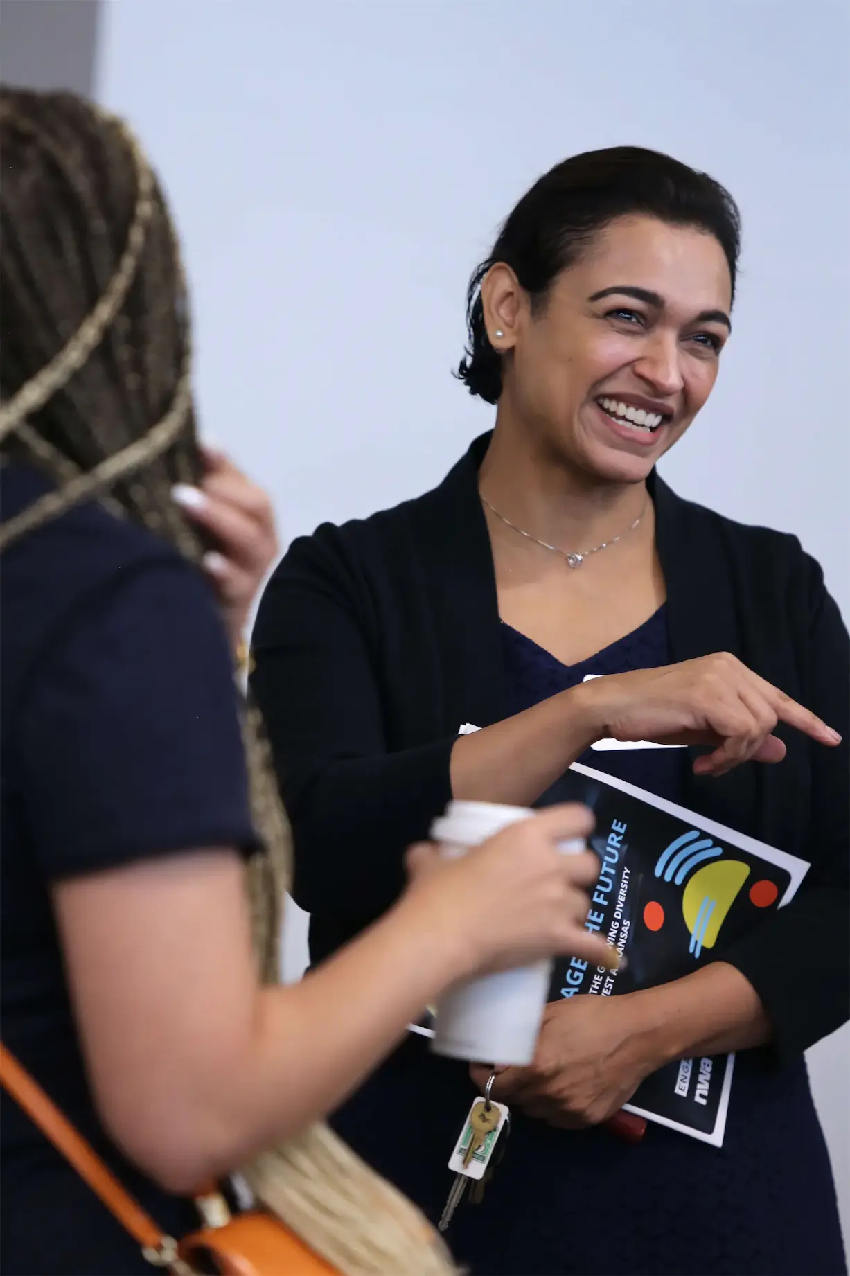 Smiling women at a networking event, one holding a coffee cup and a book titled Engage the Future.