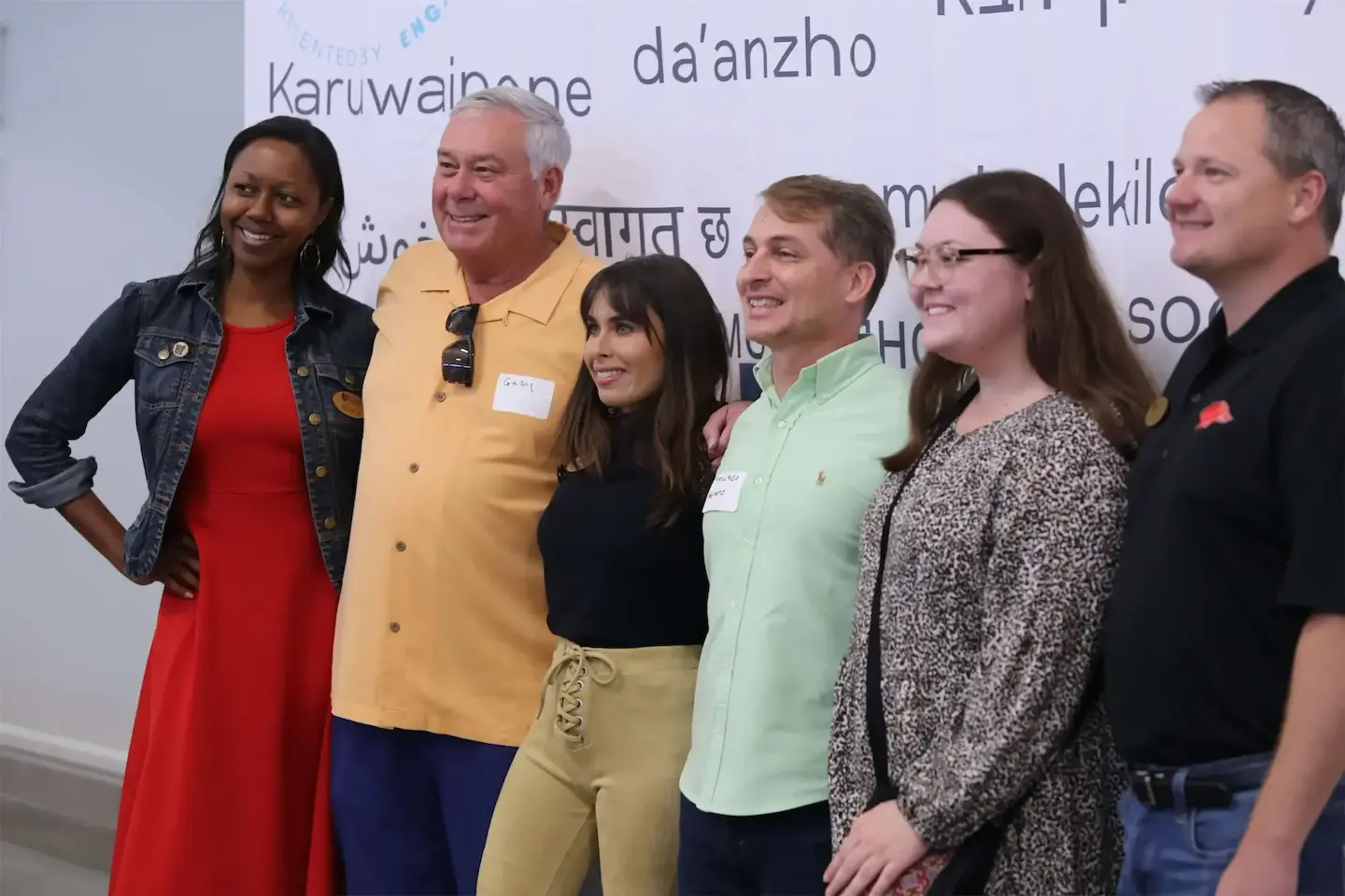 Group of six people posing together at an event with a multilingual backdrop.