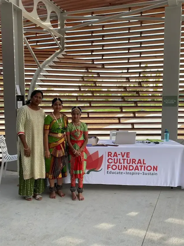 Three people in traditional attire at a Ra-Ve Cultural Foundation event booth.