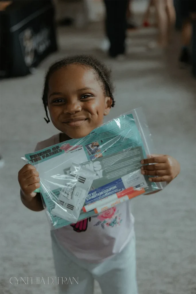 Child smiling while holding a clear bag of booklets and coupons at an event.