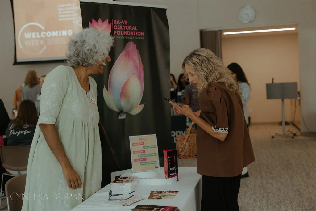 Two women engage at a cultural foundation booth during a welcoming event indoors.