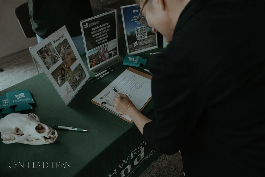 Volunteer signing a clipboard at a nature conservation event table with informational displays.