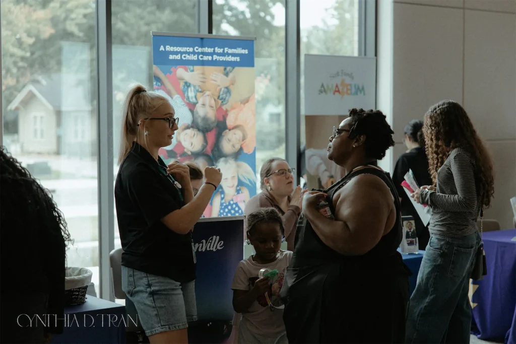 Community event with diverse individuals networking near family resource center booth.