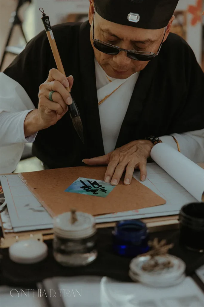Artist in traditional attire practicing calligraphy with brush and ink on paper.