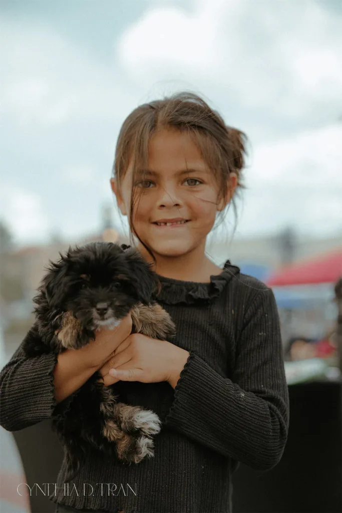 Young girl holding a fluffy black and brown puppy while smiling outdoors.