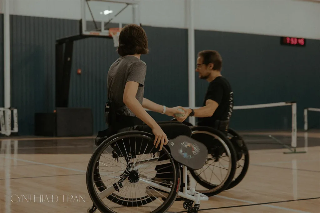 Two people in wheelchairs playing sports indoors on a court.