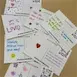 Handwritten love notes scattered on a table, decorated with hearts and colorful doodles, expressing positive messages.