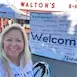 Smiling person in front of Walton's store, welcome sign visible. יום